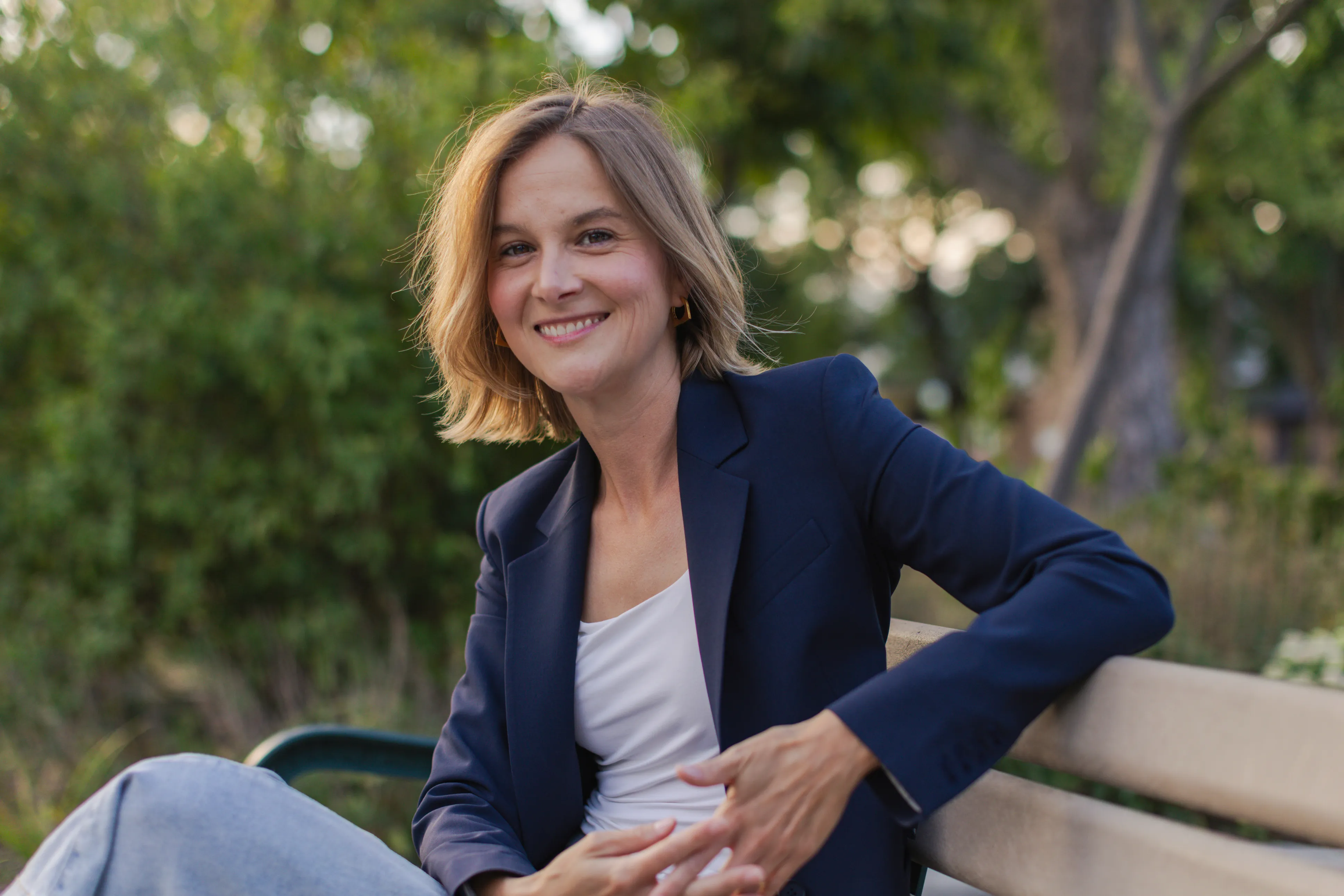Laura Dean laughing on a park bench in Toronto, one arm resting along the bench back
